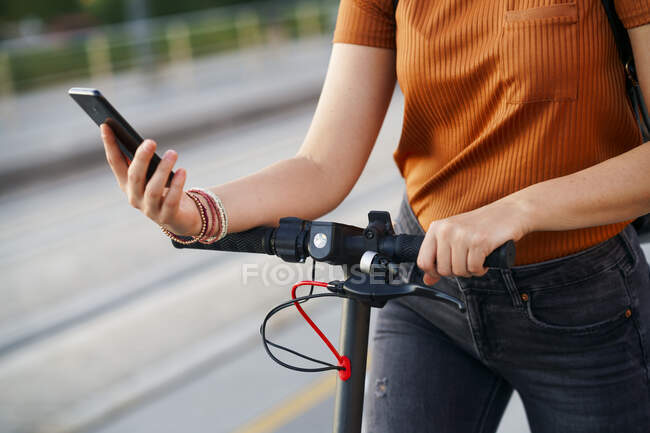 Mujer con scooter eléctrico usando smartphone, vista parcial - foto de stock