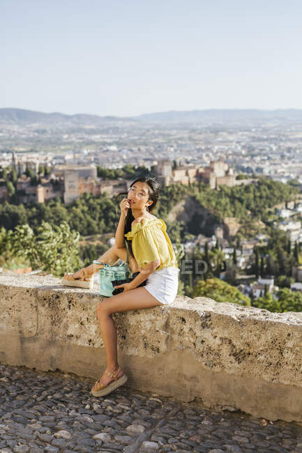 Giovane donna con macchina fotografica seduta su un muro all'Alhambra, Granada, Spagna — Foto stock