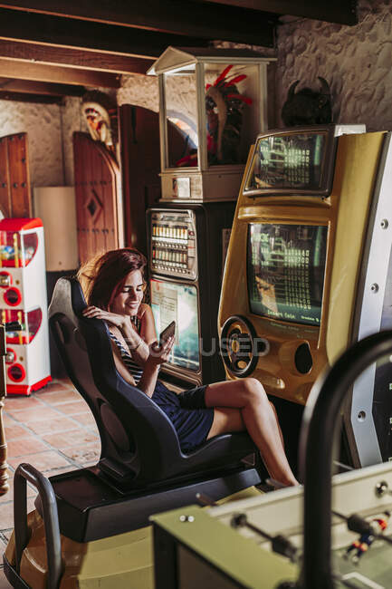 Junge Frau benutzt Handy im Fahrsimulator in Sportbar — Stockfoto