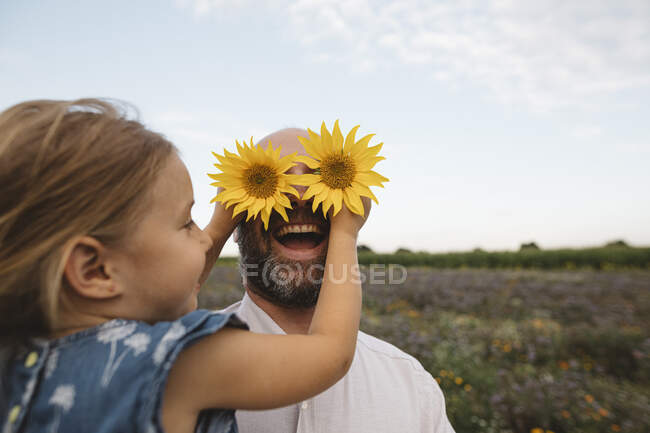 Figlia che copre occhi di padre di girasoli — Foto stock