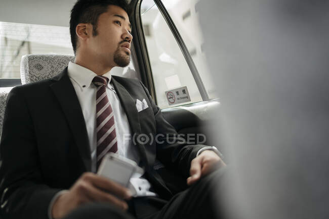 Young businessman with cell phone in a taxi looking out of window — Stock Photo