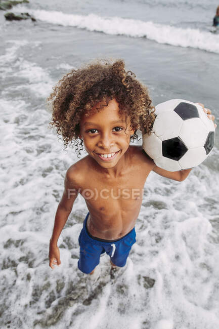 Portrait d'un garçon souriant tenant un ballon de football sur la plage — Photo de stock