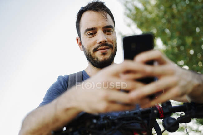 Retrato del hombre de contenido con scooter eléctrico mirando el teléfono celular - foto de stock