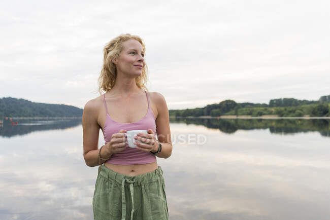 Giovane donna che beve caffè da una tazza in un lago — Foto stock