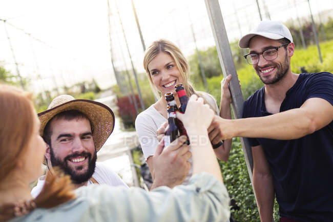 Gruppo di amici che brindano con bottiglie di birra in serra — Foto stock