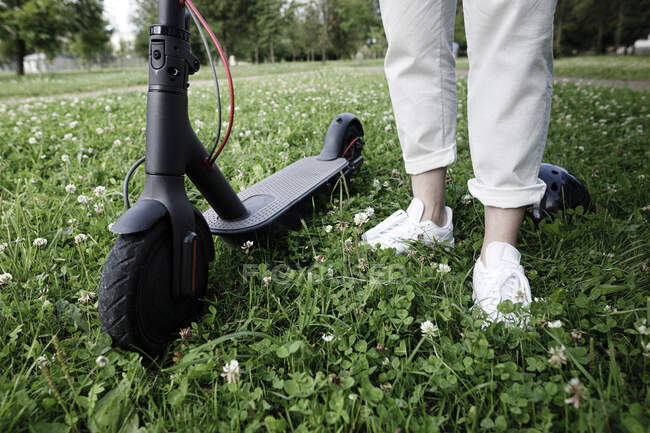 Femme avec e-scooter debout sur une prairie — Photo de stock