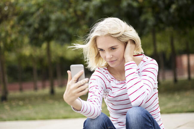 Portrait of blond woman using smartphone and taking a selfie — Stock Photo