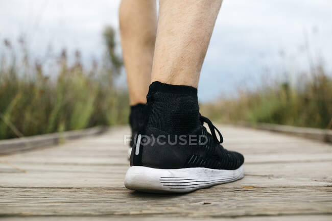 Vue arrière de chaussures de course noires, jogger mâle debout sur une passerelle en bois — Photo de stock