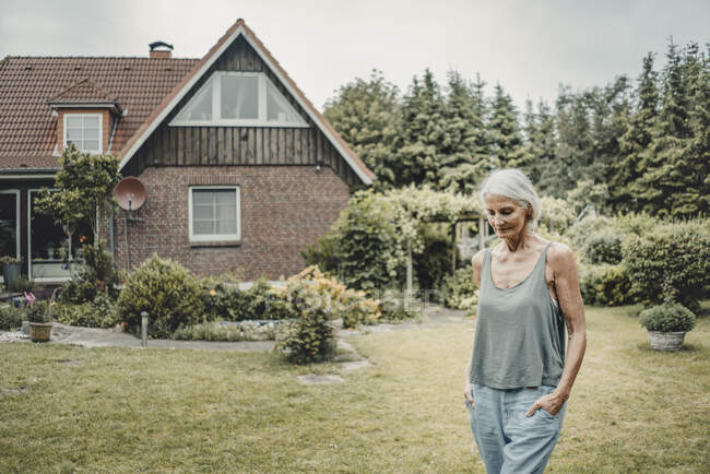 Старша жінка йде по саду, тримаючи руки в кишенях. — стокове фото