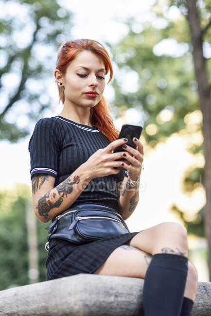 Portrait of red-haired tattooed woman using cell phone outdoors — Stock Photo