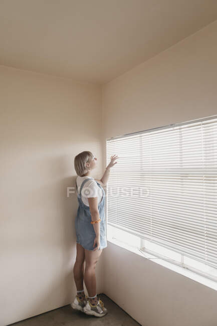 Junge Frau blickt durch Jalousien zum Fenster — Stockfoto