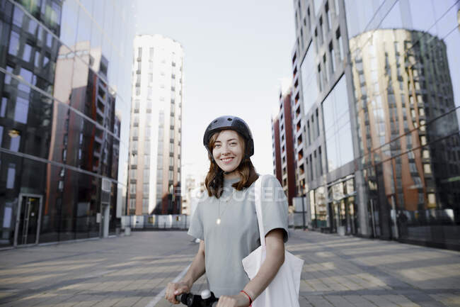 Жінка з електронним скутером і шолом, сучасні офісні будівлі на задньому плані — стокове фото