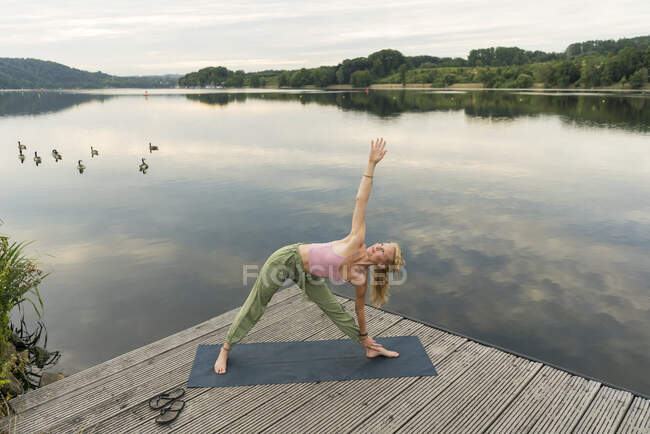 Jovem fazendo ginástica em um molhe em um lago — Fotografia de Stock