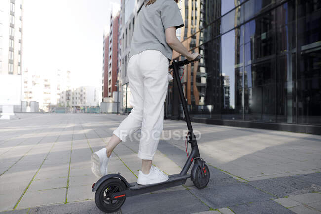 Giovane donna su e-scooter, edifici moderni sullo sfondo — Foto stock