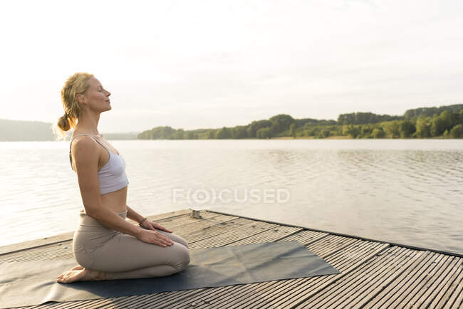 Mujer joven practicando yoga en un embarcadero en un lago - foto de stock
