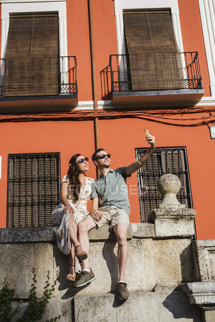 Пара сидить на стіні, тримаючи самовіддані смартфон (Гранада, Іспанія). — стокове фото