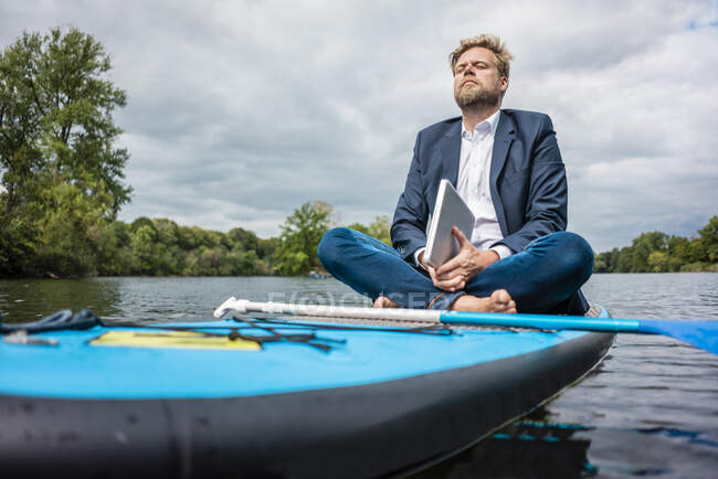 Businessman with laptop sitting on SUP board on a lake — Stock Photo