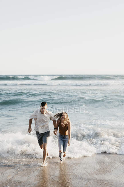 Счастливая молодая пара бежит к берегу моря — стоковое фото