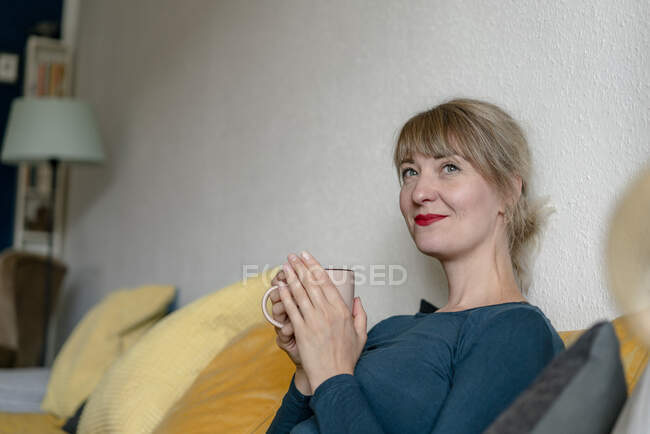 Portrait of smiling woman sitting on the couch with a cup of coffee — Stock Photo