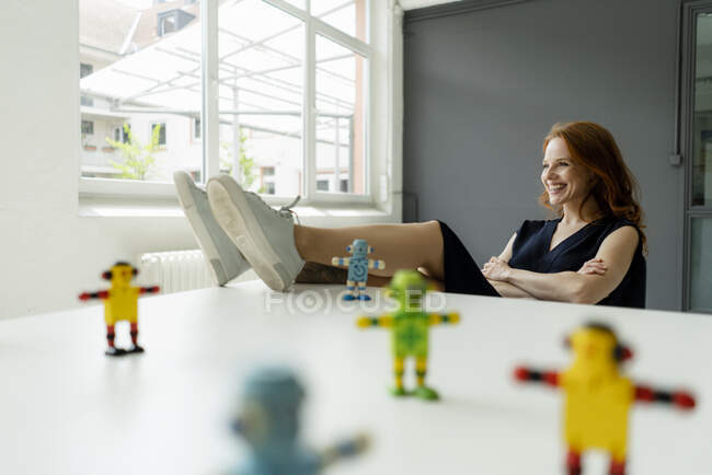 Портрет рудої жінки на горищі з мініатюрними роботами на столі. — стокове фото