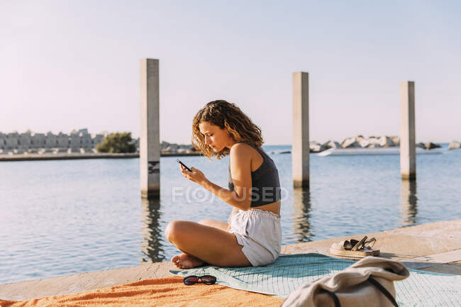 Junge Frau sitzt mit Smartphone auf Seebrücke — Stockfoto