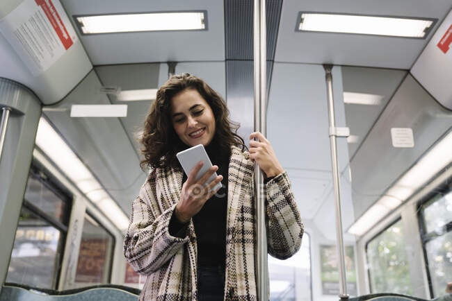 Jovencita sonriente usando smartphone en un metro - foto de stock