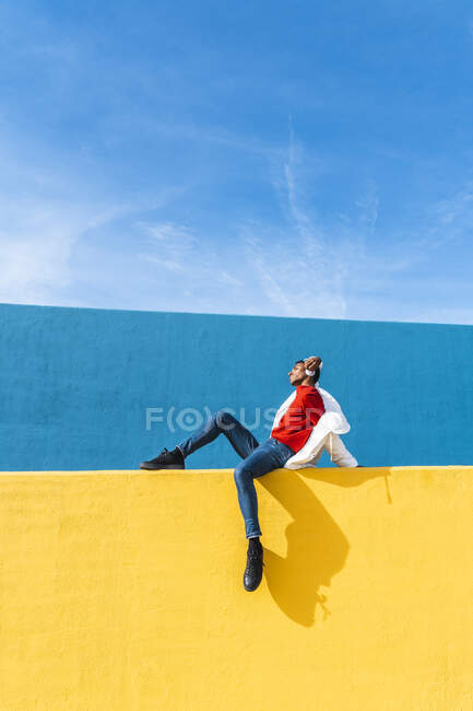 Giovane ballerina seduta sul muro giallo, ascoltando musica — Foto stock