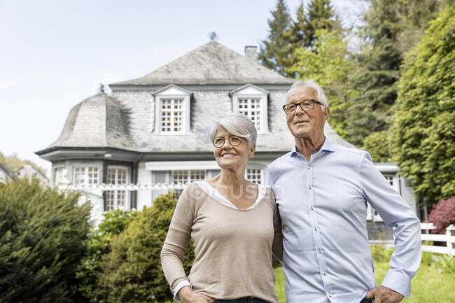Sonriente pareja de ancianos de pie en el jardín de su casa - foto de stock