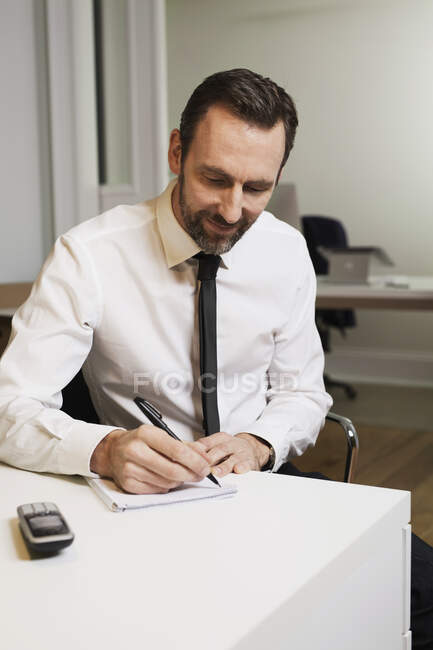 Empresario sentado en el escritorio en la oficina tomando notas - foto de stock