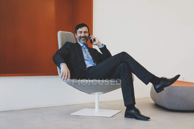 Smiling mature businessman sitting in chair talking on cell phone — Stock Photo