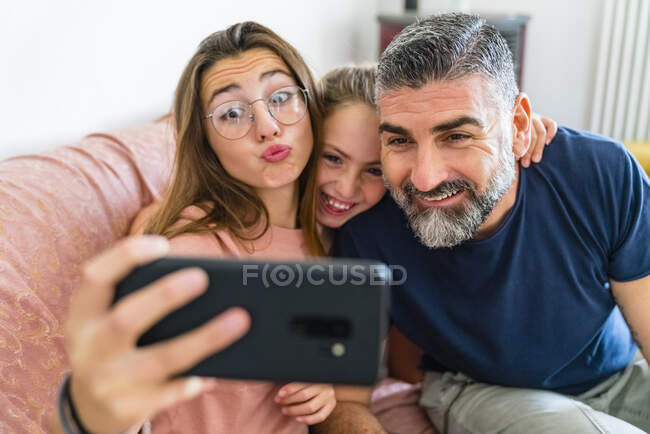 Glücklicher Vater mit zwei Töchtern beim Selfie auf der heimischen Couch — Stockfoto