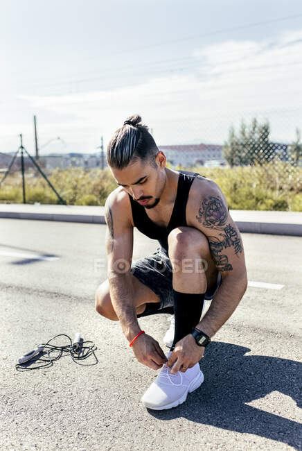 Sporty giovane uomo legare scarpe prima di formazione su una strada — Foto stock