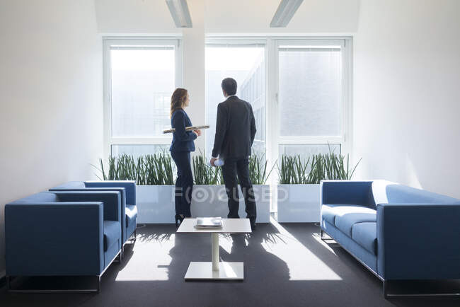 Businesswoman and businessman looking out of window in office lounge — Stock Photo