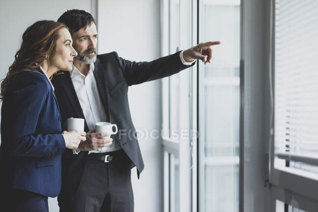 Businesswoman and businessman in office looking out of window — Stock Photo