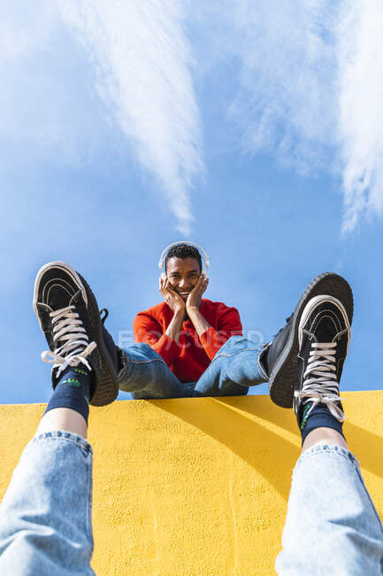 Young man with headphones, dancing for person, leaning on yellow wall — Stock Photo
