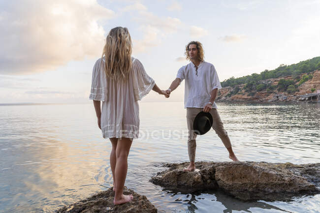 Junges Paar auf Felsen vor dem Meer, Händchen haltend, Ibiza, Balearen, Spanien — Stockfoto