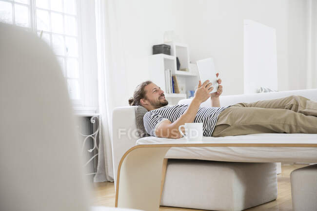 Молодий чоловік лежав удома на дивані з планшетом. — стокове фото
