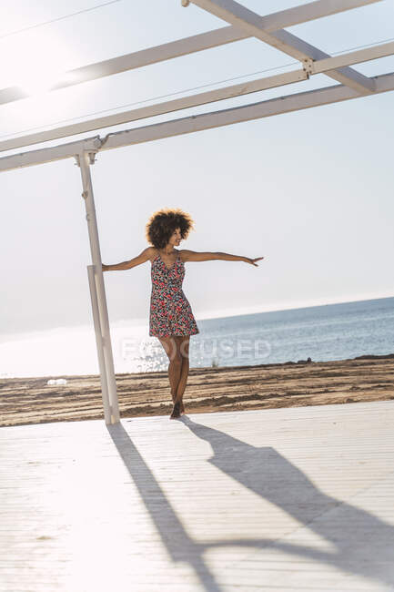 Jovem mulher vestindo vestido de verão desfrutando da luz solar em um terraço na praia — Fotografia de Stock