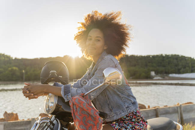 Jeune femme assise sur scooter moteur au coucher du soleil, Ibiza — Photo de stock