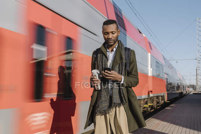 Портрет стильного чоловіка, що використовує смартфон поруч із поїздом — стокове фото