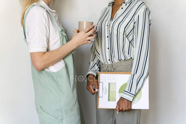 Обрезанный вид на двух женщин с бумагой и чашкой кофе — стоковое фото