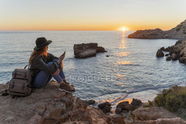 Mujer joven usando smartphone en la playa al atardecer, Ibiza - foto de stock