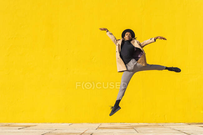Giovane che balla davanti al muro giallo, saltando a mezz'aria — Foto stock
