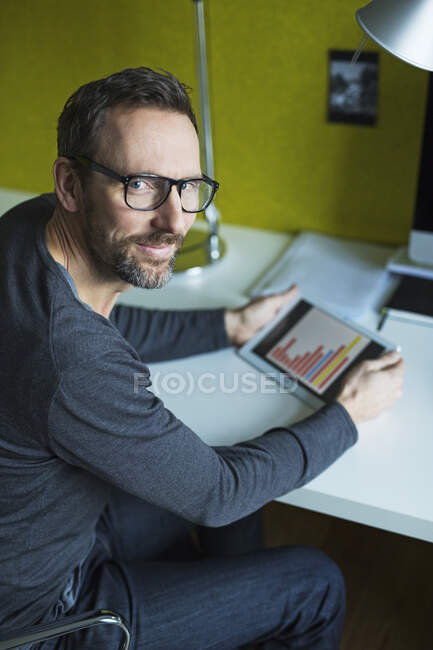 Retrato de hombre de negocios confiado usando tableta en el escritorio en la oficina - foto de stock