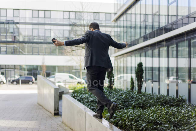 Rückansicht eines Geschäftsmannes, der vor einem Bürogebäude an einer Wand balanciert — Stockfoto