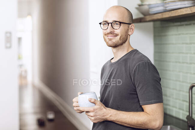 Hombre con una taza de pie en la mañana en casa en la cocina - foto de stock
