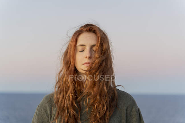 Рыжая молодая женщина с закрытыми глазами на побережье на закате, Ибица, Испания — стоковое фото