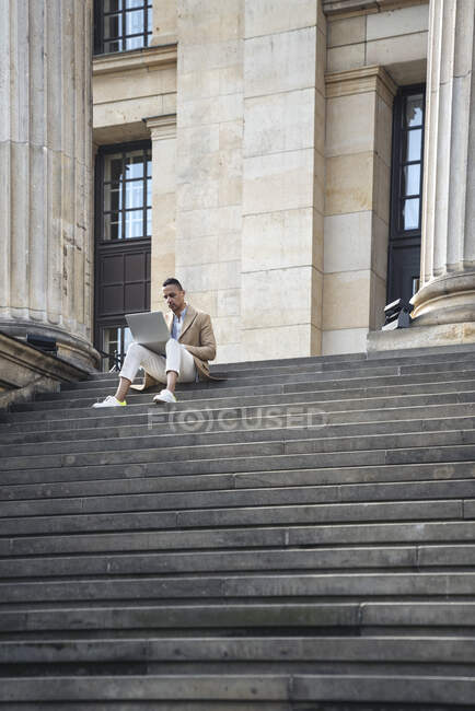 Businessman sitting on stairs using laptop — Stock Photo