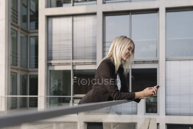 Blonde Geschäftsfrau nutzt Smartphone im Hintergrund modernes Gebäude — Stockfoto