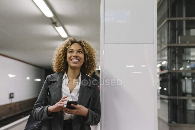 Happy woman with cell phone waiting in subway station — Stock Photo